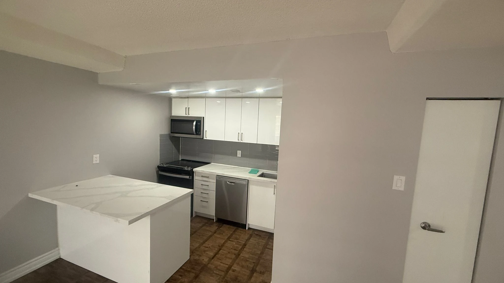 Finished MIRG kitchen renovation with white gloss cabinetry, a white peninsula with a stone-look countertop, a grey tiled backsplash and recessed lighting